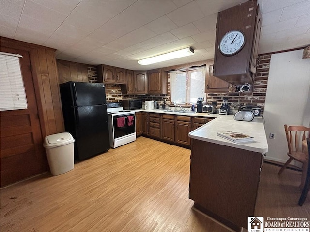 kitchen featuring electric stove, light hardwood / wood-style flooring, black refrigerator, and kitchen peninsula