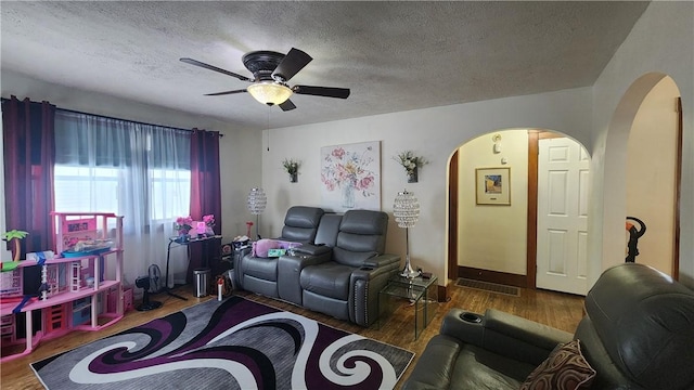 living room featuring ceiling fan, dark wood-type flooring, and a textured ceiling