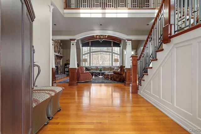 foyer with a towering ceiling, a fireplace, decorative columns, and light wood-type flooring