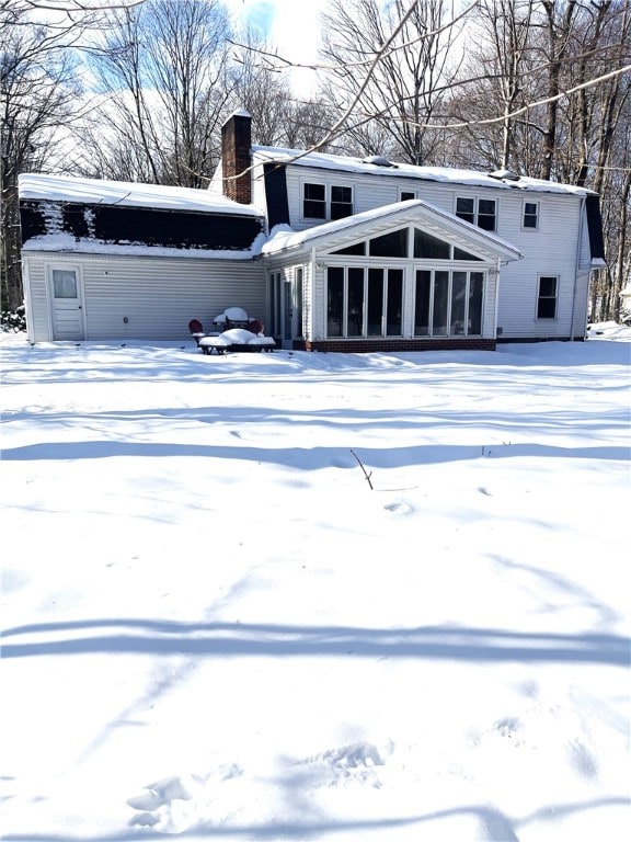 snow covered back of property with a sunroom