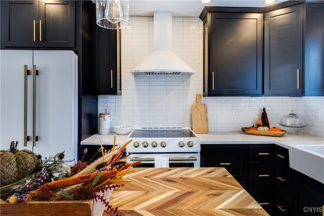 kitchen with wall chimney range hood, white electric range oven, high quality fridge, decorative backsplash, and decorative light fixtures