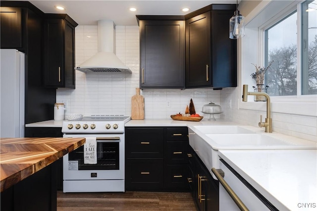 kitchen with sink, white appliances, hanging light fixtures, backsplash, and wall chimney exhaust hood