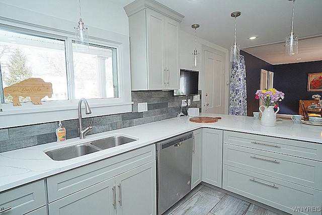 kitchen with light stone counters, stainless steel dishwasher, decorative light fixtures, and sink