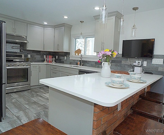 kitchen with sink, a breakfast bar, appliances with stainless steel finishes, hanging light fixtures, and kitchen peninsula