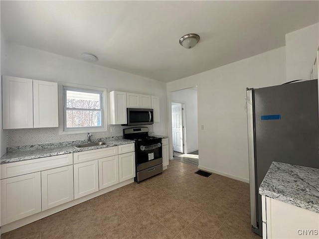 kitchen with tasteful backsplash, sink, white cabinets, light stone counters, and stainless steel appliances