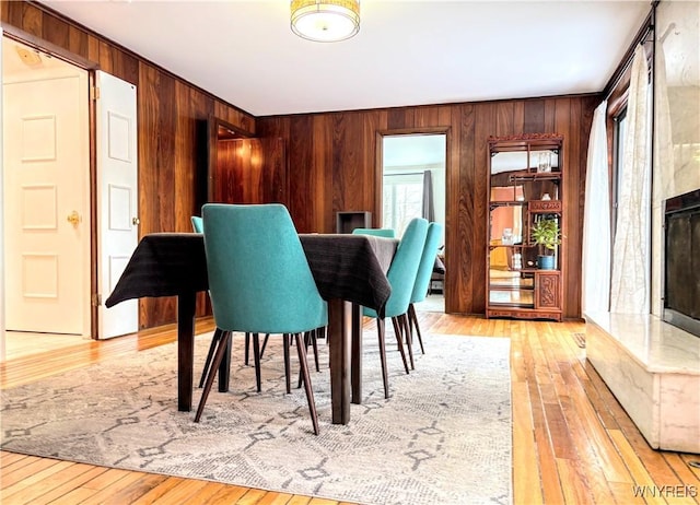 dining space featuring a premium fireplace, wood walls, and light hardwood / wood-style flooring