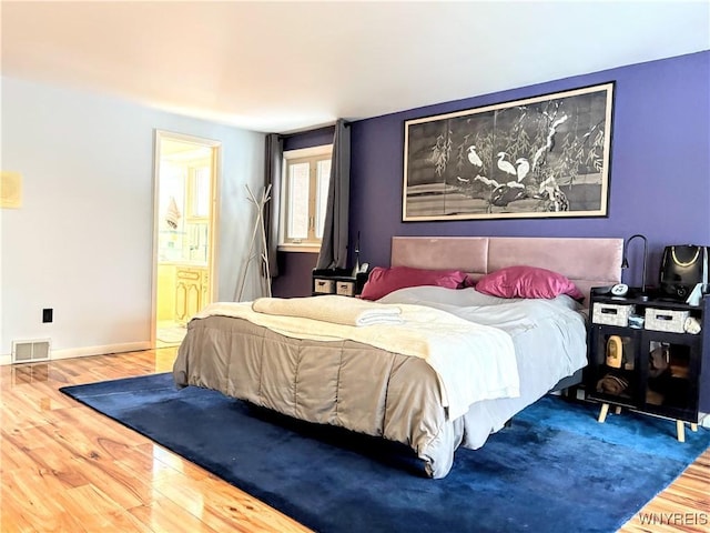 bedroom with ensuite bathroom and hardwood / wood-style floors