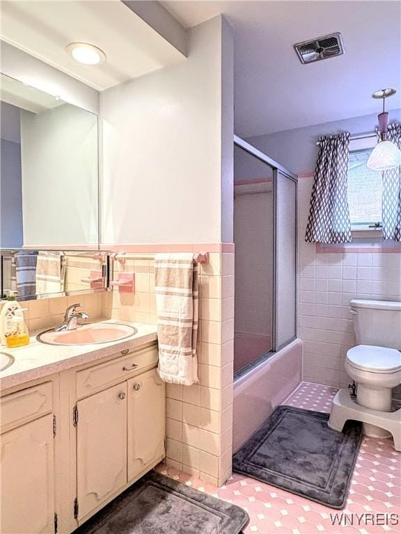 full bathroom with vanity, tile walls, bath / shower combo with glass door, and toilet