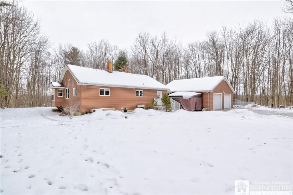 snow covered back of property with a garage and an outdoor structure