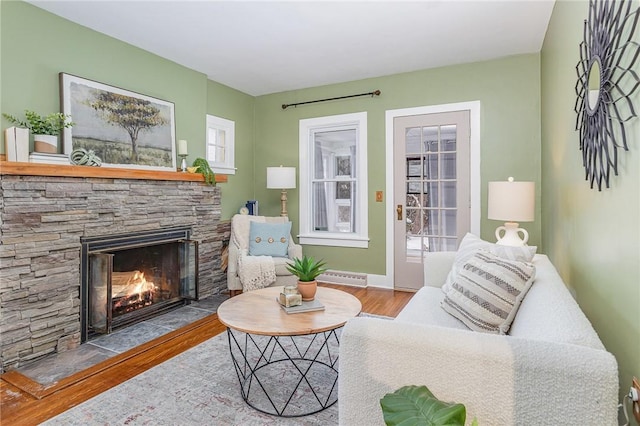 living room with baseboard heating, a stone fireplace, and light hardwood / wood-style flooring