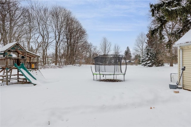 snowy yard featuring a playground and a trampoline