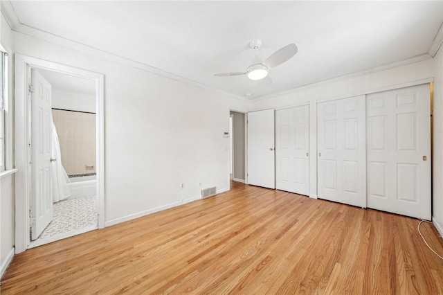 unfurnished bedroom with ensuite bath, ornamental molding, multiple closets, and light wood-type flooring