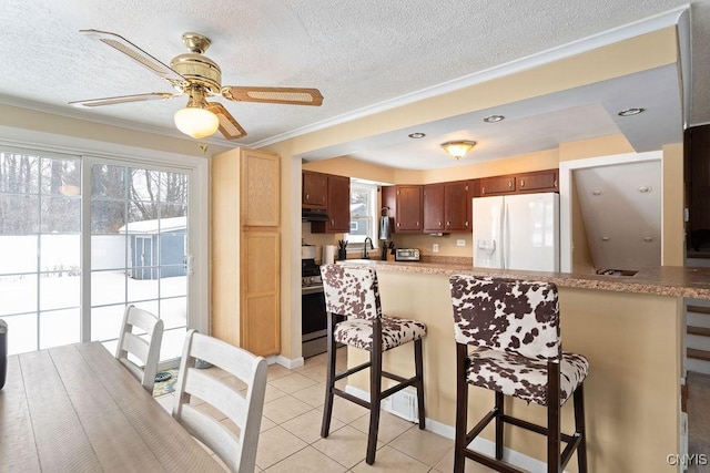 kitchen with light tile patterned flooring, stainless steel gas stove, white refrigerator with ice dispenser, kitchen peninsula, and a textured ceiling