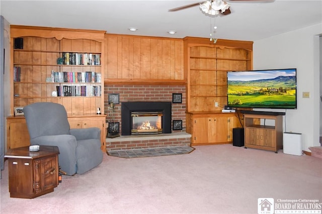 carpeted living room featuring a brick fireplace, ceiling fan, and wood walls