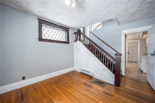 stairs with baseboard heating, a textured ceiling, and hardwood / wood-style flooring