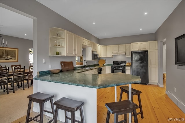 kitchen featuring light hardwood / wood-style flooring, a kitchen breakfast bar, black appliances, kitchen peninsula, and cream cabinetry