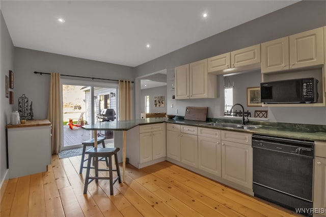 kitchen with sink, a breakfast bar area, light hardwood / wood-style floors, black appliances, and kitchen peninsula