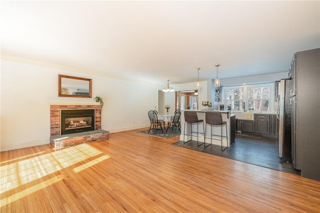 living room with a notable chandelier, ornamental molding, a brick fireplace, and light wood-type flooring