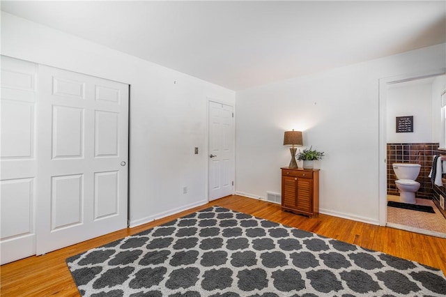 bedroom featuring hardwood / wood-style flooring, a closet, ensuite bathroom, and tile walls