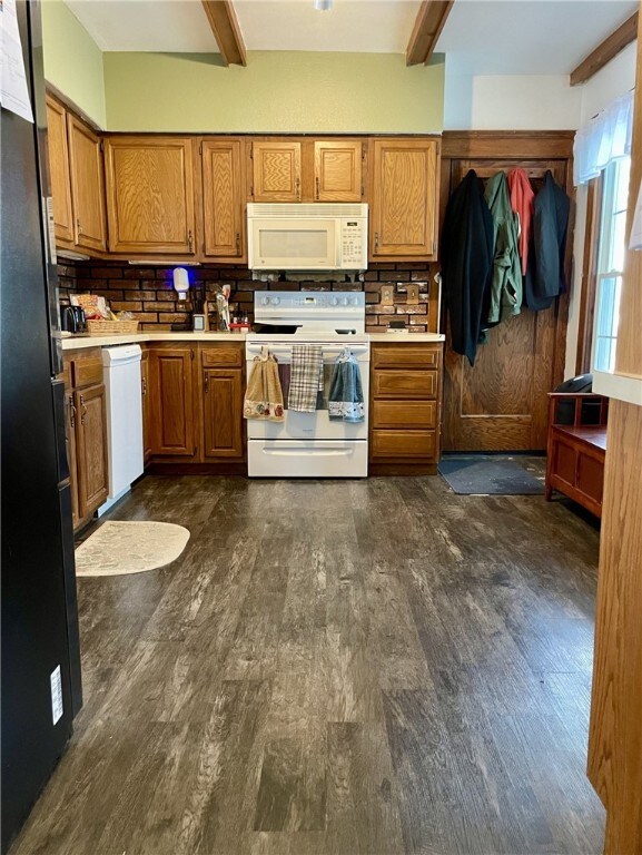 kitchen with beam ceiling, white appliances, brown cabinets, and dark wood finished floors