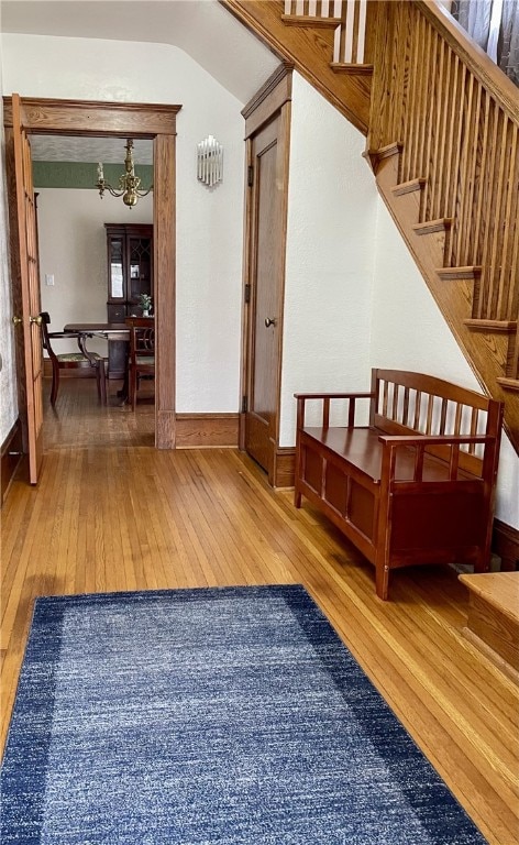 entrance foyer with stairway, baseboards, an inviting chandelier, lofted ceiling, and hardwood / wood-style flooring