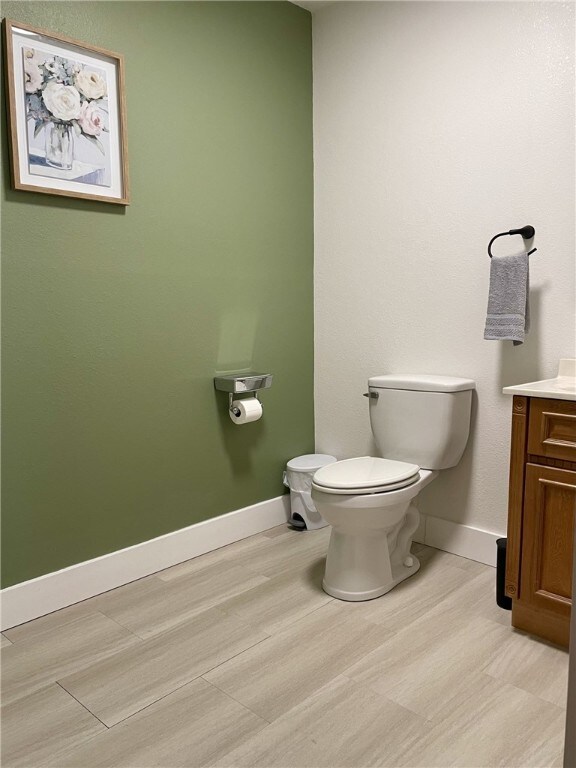 bathroom with baseboards, toilet, wood finished floors, and vanity