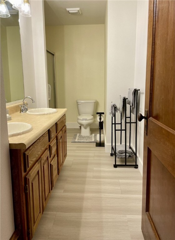 full bathroom featuring baseboards, visible vents, double vanity, a sink, and toilet