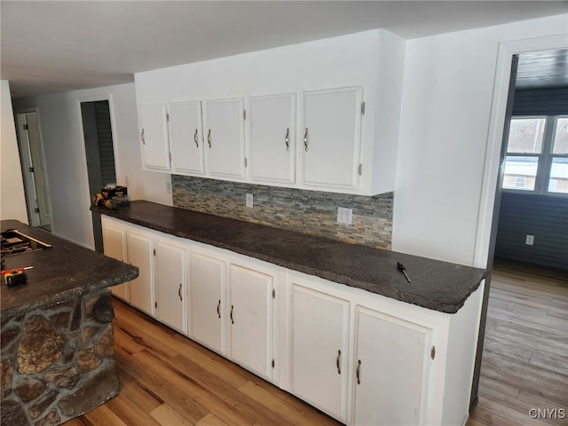 kitchen with tasteful backsplash, dark stone countertops, white cabinets, and light wood-type flooring