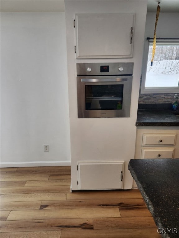 kitchen featuring decorative light fixtures, oven, light hardwood / wood-style floors, and white cabinets