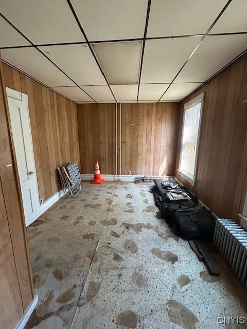 interior space with radiator heating unit, a drop ceiling, and wood walls