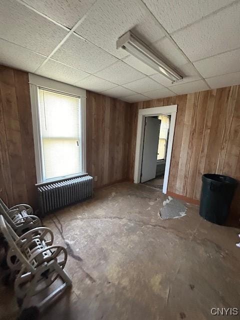 miscellaneous room with a drop ceiling, radiator, and wood walls