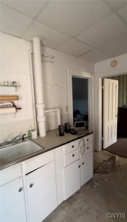 kitchen with sink, a paneled ceiling, and white cabinets