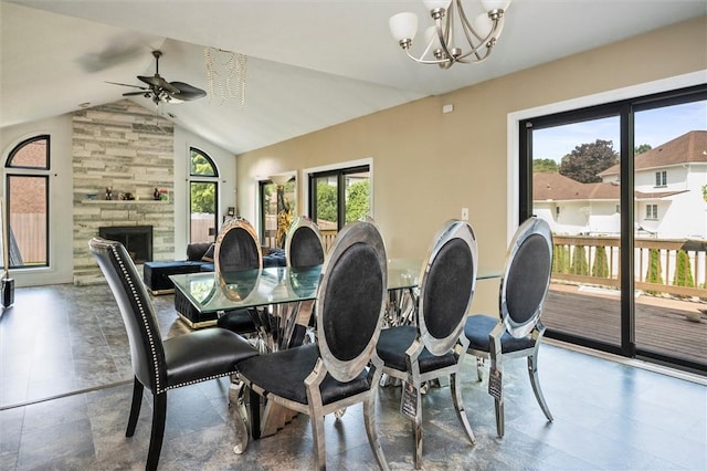 dining area with a stone fireplace, a wealth of natural light, ceiling fan with notable chandelier, and vaulted ceiling