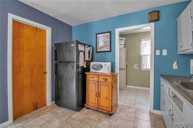 kitchen with black fridge, light tile patterned flooring, sink, and white cabinets