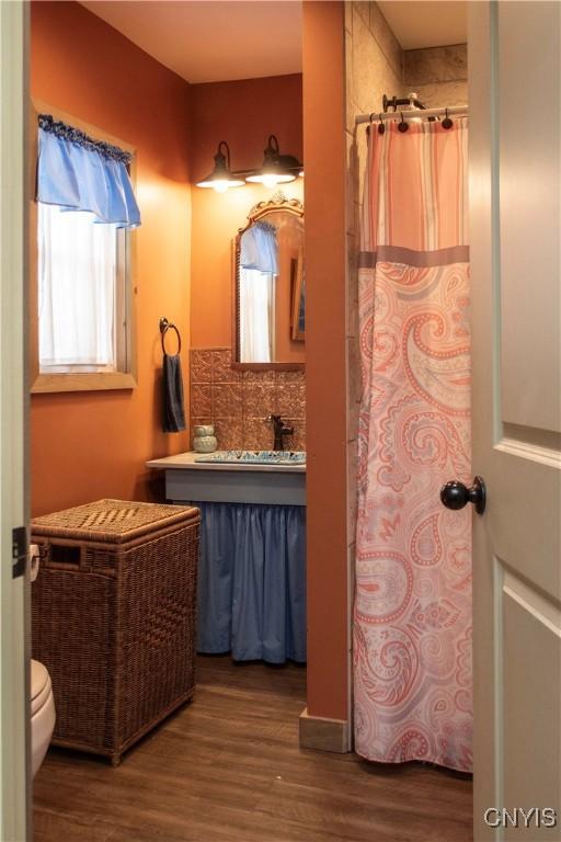 bathroom featuring toilet, vanity, curtained shower, hardwood / wood-style floors, and backsplash