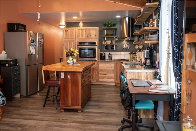 kitchen featuring a breakfast bar, light brown cabinetry, a center island, stainless steel appliances, and wall chimney range hood