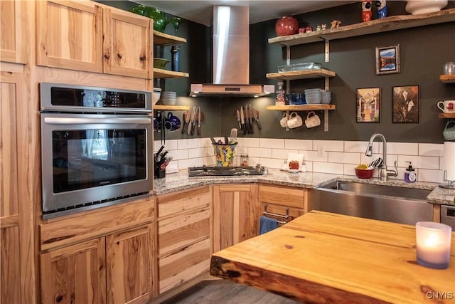 kitchen featuring stainless steel appliances, sink, wall chimney range hood, and light stone counters