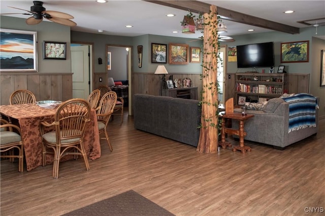 dining space with beam ceiling, wood-type flooring, wooden walls, and ceiling fan