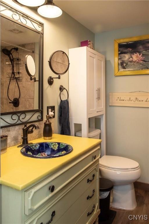 bathroom featuring hardwood / wood-style flooring, vanity, a tile shower, and toilet