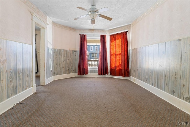 unfurnished room featuring ceiling fan, wooden walls, a textured ceiling, and carpet