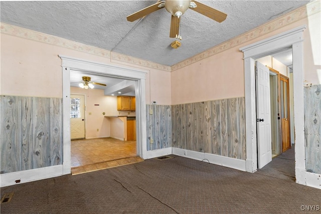 spare room with ceiling fan, carpet, a textured ceiling, and wood walls