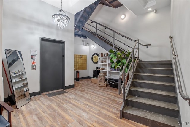 stairs featuring a towering ceiling, wood-type flooring, a chandelier, and elevator