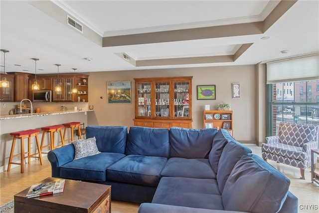 living room featuring a tray ceiling, crown molding, and light wood-type flooring