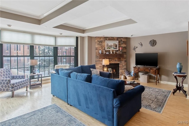 living room with hardwood / wood-style flooring, crown molding, a stone fireplace, and a raised ceiling