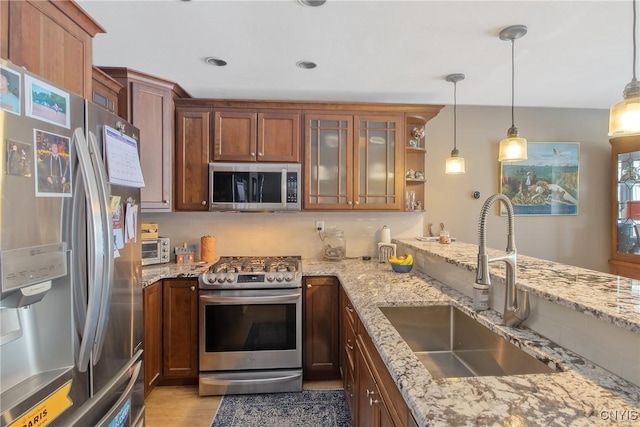 kitchen featuring light stone counters, appliances with stainless steel finishes, decorative light fixtures, and sink