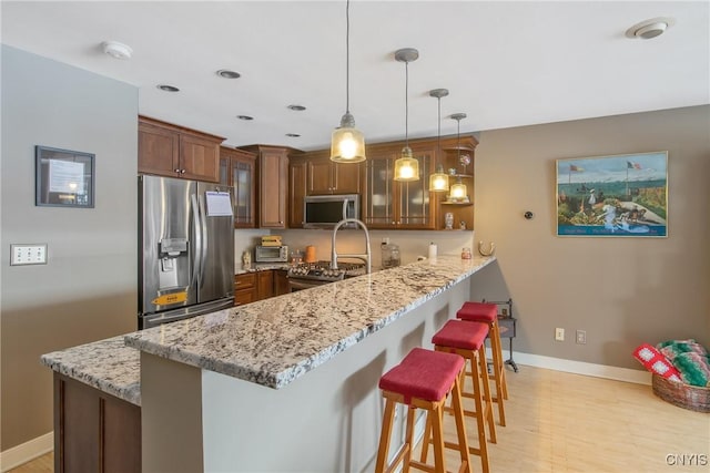 kitchen with a kitchen bar, light stone counters, hanging light fixtures, kitchen peninsula, and stainless steel appliances