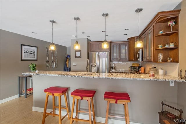 kitchen with a kitchen bar, light stone counters, hanging light fixtures, kitchen peninsula, and stainless steel appliances