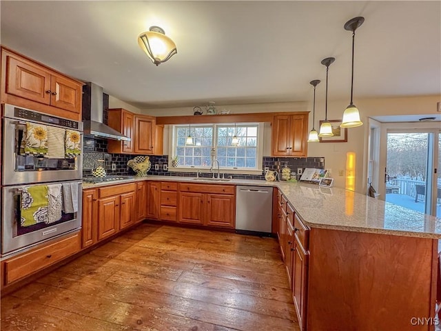 kitchen with pendant lighting, sink, kitchen peninsula, stainless steel appliances, and wall chimney range hood