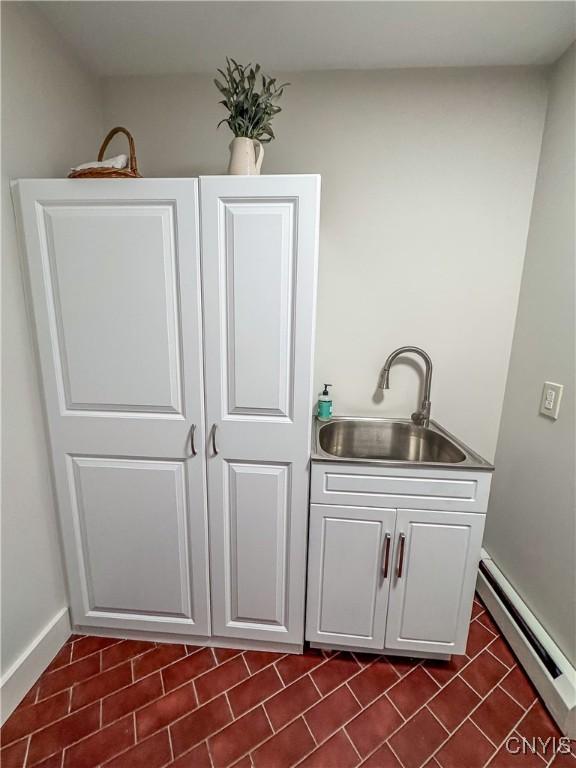 bar featuring white cabinetry, sink, and baseboard heating