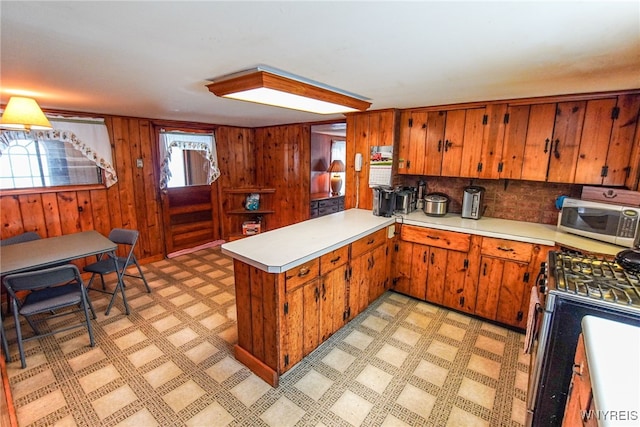 kitchen with wood walls, backsplash, kitchen peninsula, and appliances with stainless steel finishes